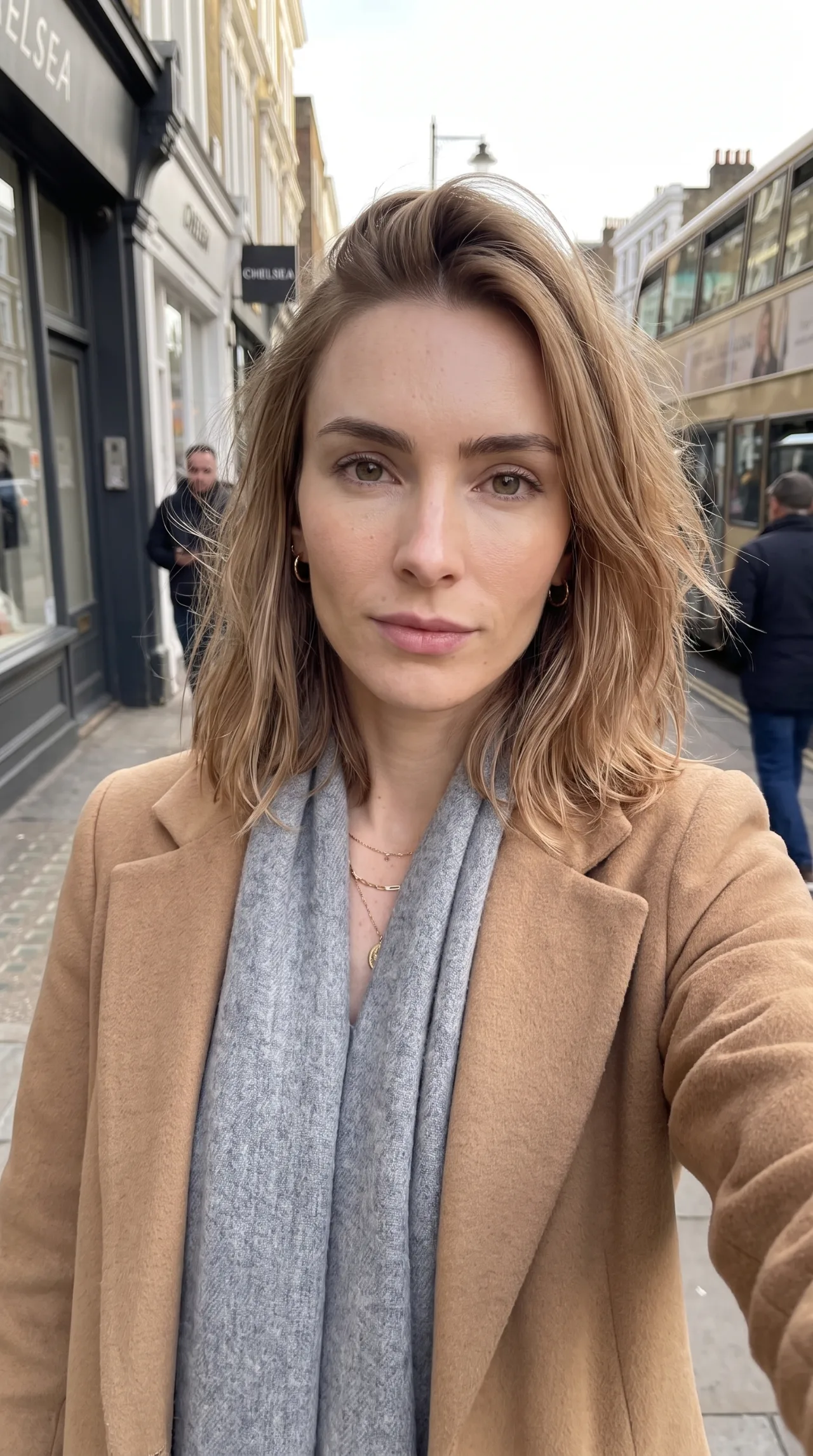 A woman in a camel coat and grey scarf on a London street